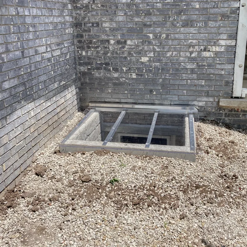 Window well cover on dark brick home with gravel surround