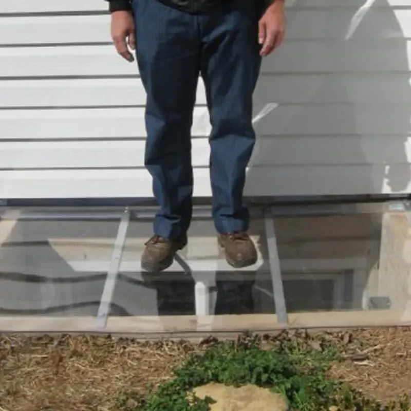 Adult standing on a window well cover to demonstrate its strength